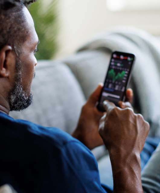 Man sitting on a couch checking his crypto wallet on a smartphone.